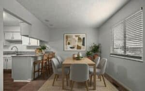 A modern dining room with a wooden table, six chairs, abstract wall art, indoor plants, and a view into a white kitchen with a breakfast bar and three stools.