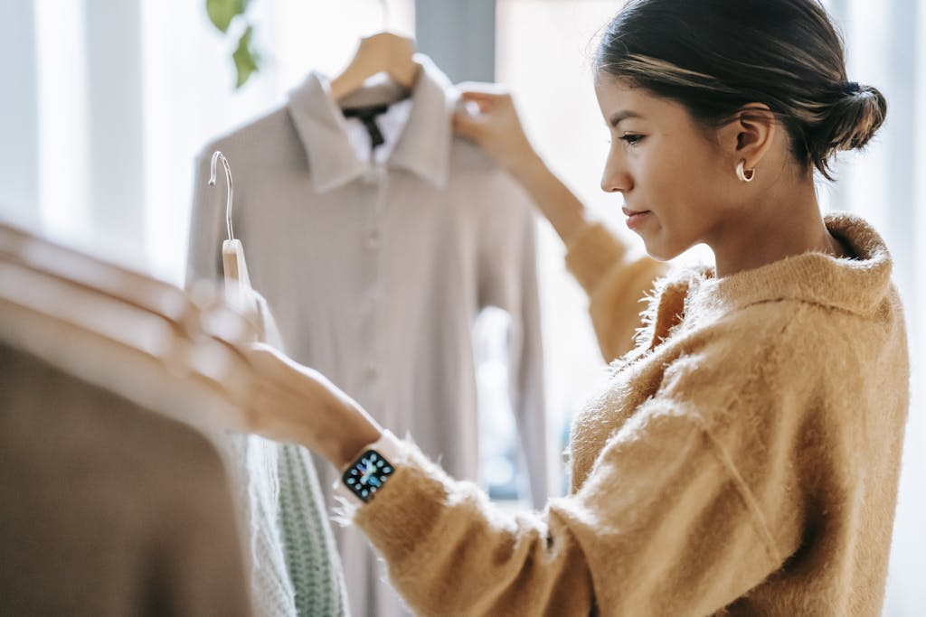 Crop focused ethnic female in casual clothes choosing apparel while standing near rack in boutique