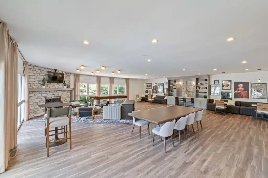 Spacious lounge with wood flooring, stone fireplace, modern furniture, long dining table, lounge chairs, wall art, and large windows letting in natural light.